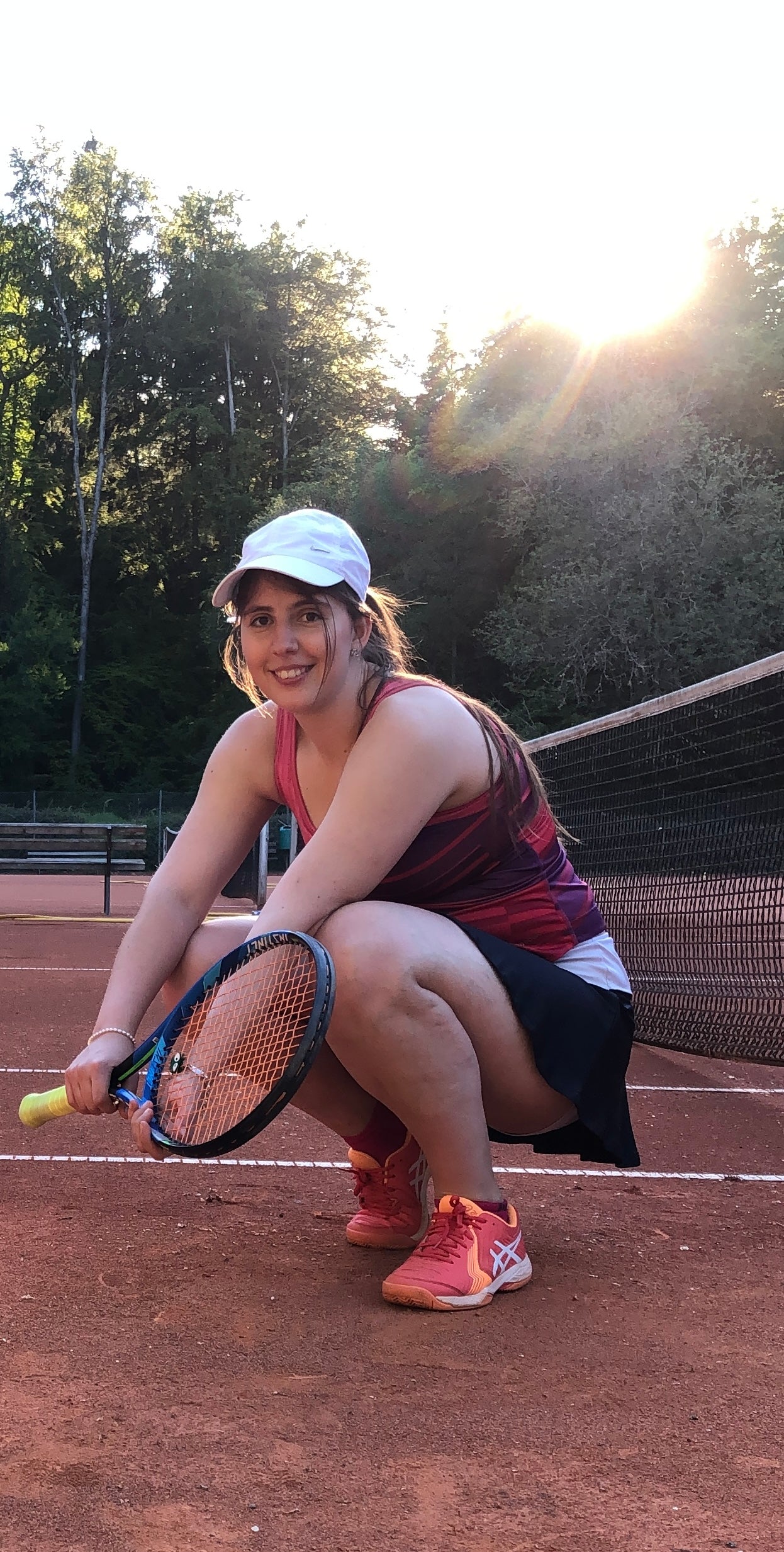 Eine Tennisspielerin sitzt in der Hocke vor einem Netz auf dem Tennisplatz aus Asche