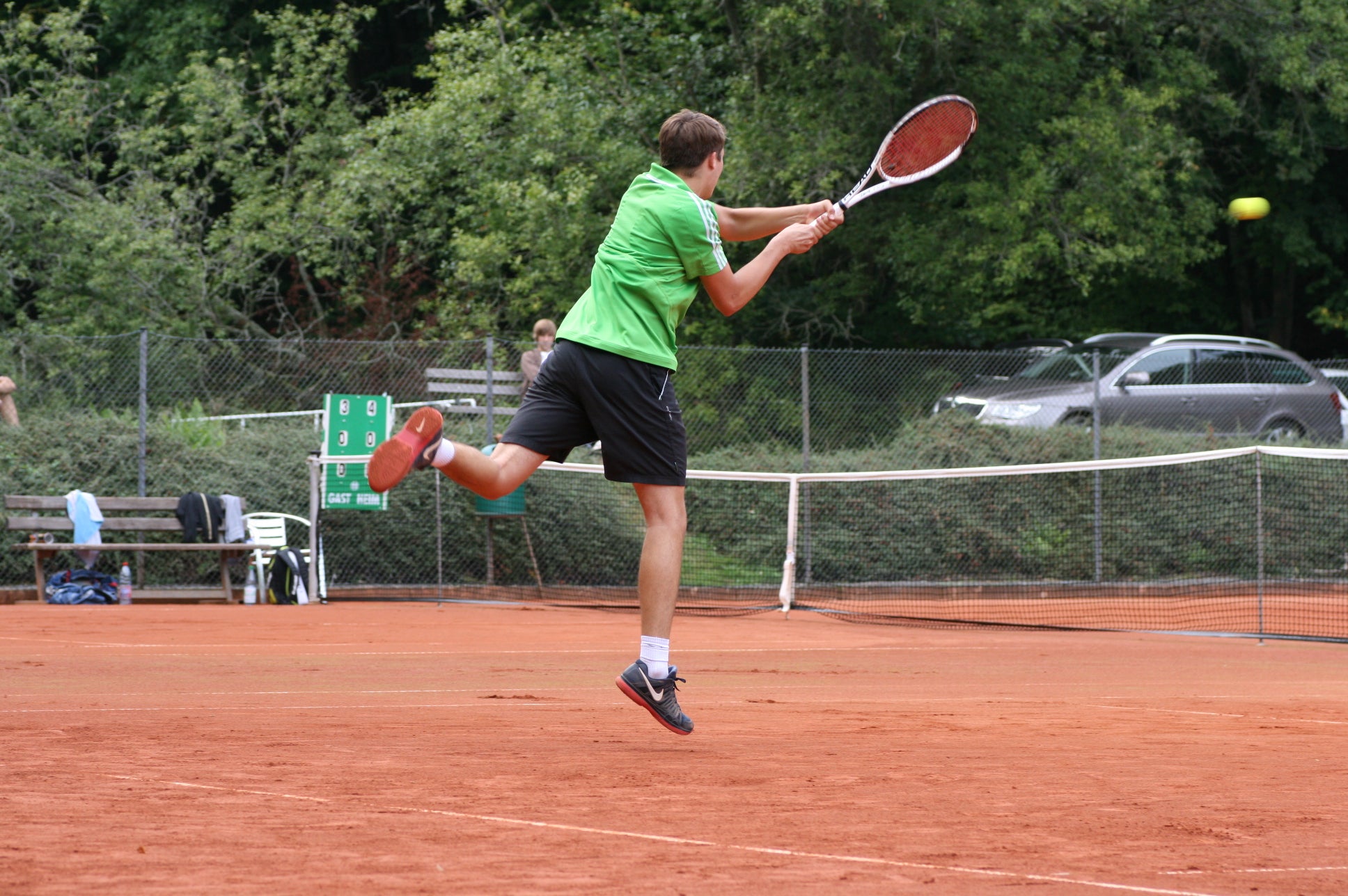 Ein Tennisspieler springt auf einem Ascheplatz hoch und spielt auf dem Platz einen seitlichen Volley