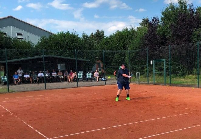 Ein Tennisspieler steht auf dem Platz und spielt den Ball mit einer Rückhand zurück