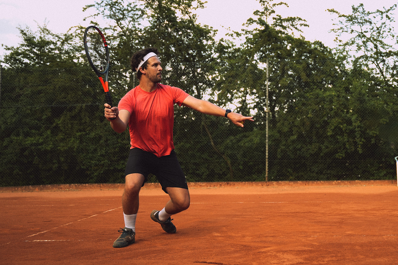 Ein Tennisspieler geht in die Knie und holt zum Schlag aus. In der rechten Hand hält er den Schläger.