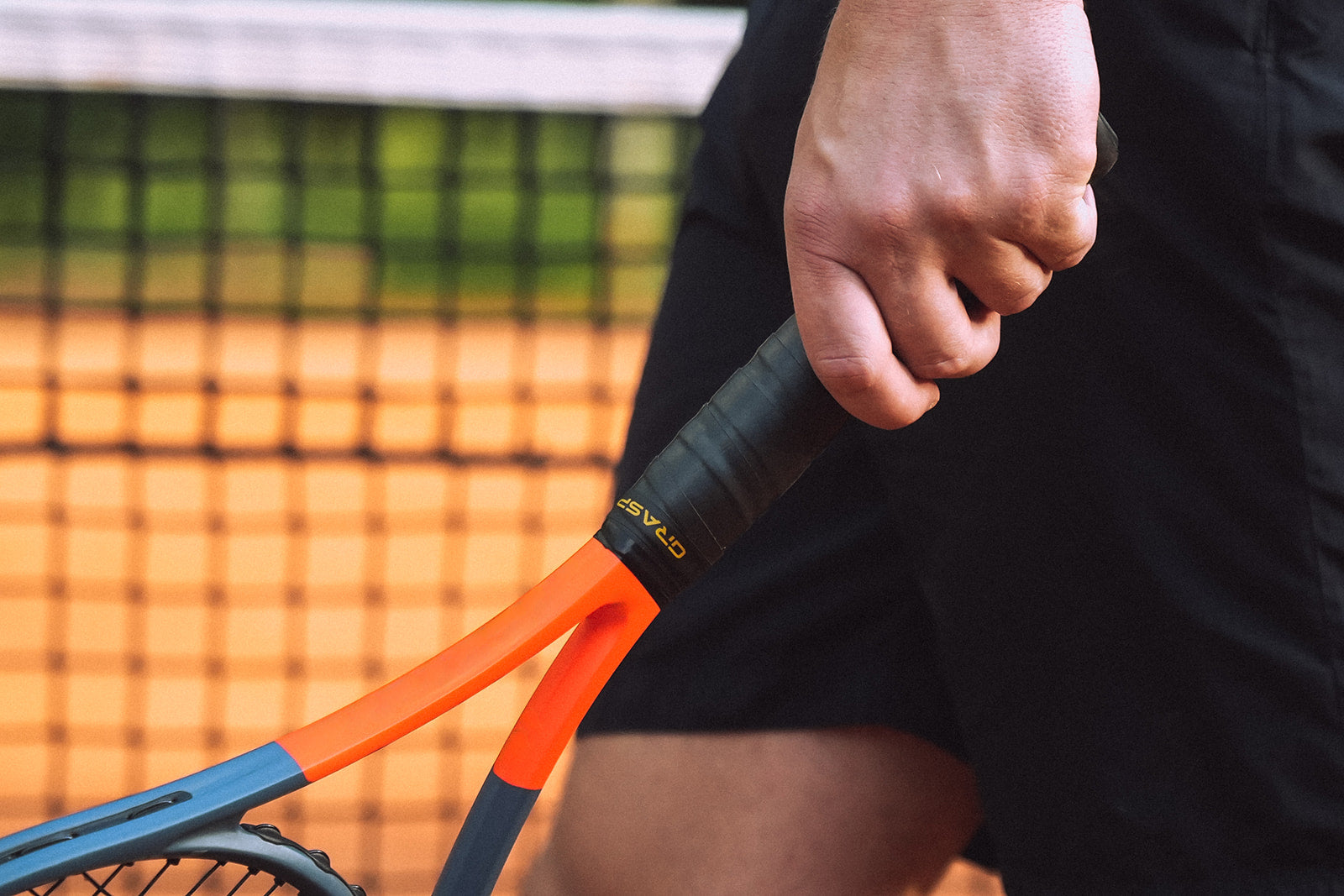 Ein Mann geht an einem Tennisnetz vorbei und hält einen Tennisschläger in seiner linken Hand.